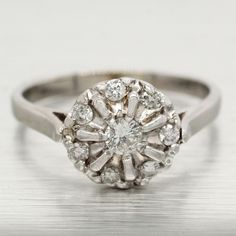 an antique diamond cluster ring on a shiny surface, with the center setting surrounded by smaller round diamonds