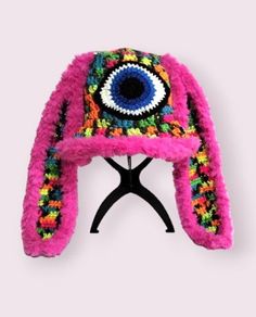 a pink hat with an eye on the front and multicolored yarn around it