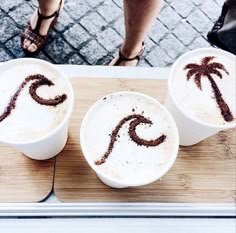 three white cups with brown designs on them sitting on a table next to a woman's legs