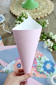 a person holding up a paper cone on top of a wooden table next to flowers