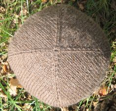 a brown knitted hat laying on top of the grass in the sun with leaves around it