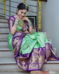 a woman in a green and purple sari sitting on steps with her hand on her chin