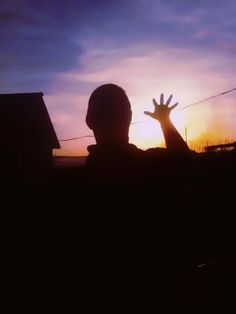 the silhouette of a person with their hands up in front of a sunset sky and clouds