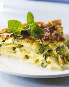 a white plate topped with a slice of quiche covered in cheese and green leafy garnish