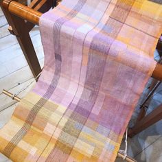 an orange and pink checkered blanket on a wooden chair with two knitting needles next to it