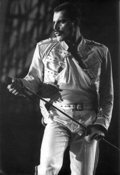 a black and white photo of a man in elvis style clothing holding a guitar on stage