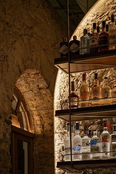 shelves filled with liquor bottles in front of a stone wall