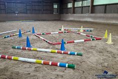 an indoor arena with many colored cones in the sand and on the ground, there is a ring made out of sticks