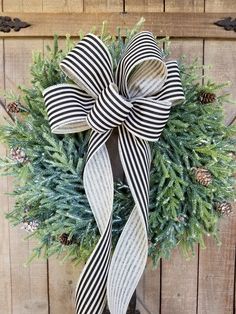 a black and white christmas wreath with pine cones, evergreens and striped ribbon hanging on a wooden door