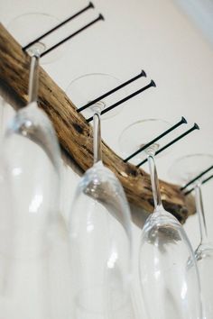 several wine glasses are lined up on a wooden stick and hang from the wall with clothes pins