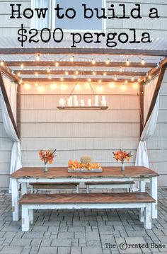 an outdoor dining area with a table and bench under the pergolated canopy that has lights strung over it