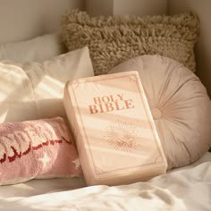 an open bible sitting on top of a bed next to two pillows and a pillow