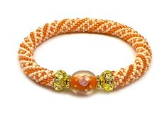 an orange and white beaded bracelet with two gold beads on the end of it