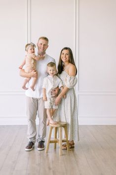 a man and woman holding two small children while standing next to each other on a stool