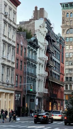 people walking down the street in front of some tall buildings with fire escapes on them