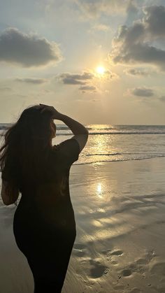 a woman standing on top of a beach next to the ocean under a cloudy sky