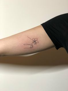 a woman's arm with a single line flower tattoo on the left inner arm