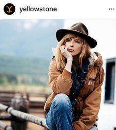 a woman sitting on a rail talking on her cell phone while wearing a cowboy hat