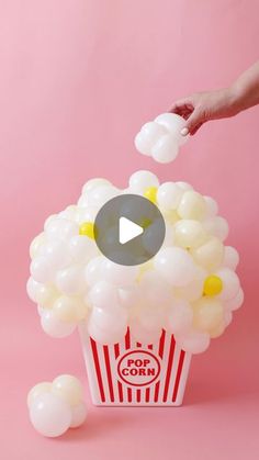 a popcorn box filled with white balloons and a hand reaching out to grab the balloon