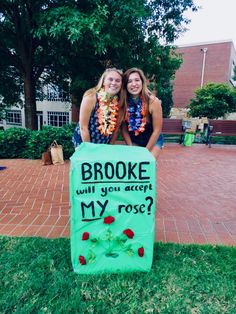 two women standing behind a sign that says brooke will you accept my rose?