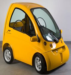 a small yellow car is parked in a room with gray flooring and white walls