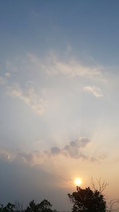 the sun is setting behind some clouds in the sky over trees and grass on an open field