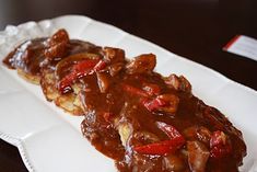 two pieces of meat covered in gravy on top of a white paper plate