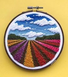 an embroidery project is displayed on a yellow surface with clouds in the sky above it