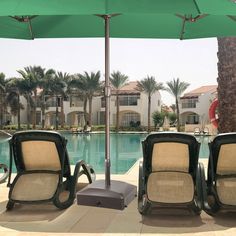 two lawn chairs sitting under an umbrella next to a swimming pool