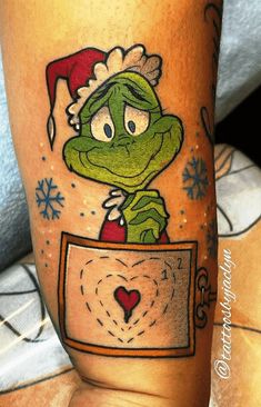 the grin face tattoo on the leg of a person wearing a santa hat and holding a heart