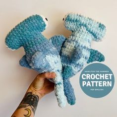 two crocheted stuffed animals in the shape of dolphins are held up by one hand