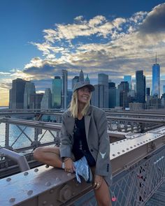 a woman sitting on the edge of a bridge in front of a cityscape