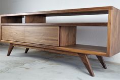 a wooden entertainment center sitting on top of a cement floor next to a white wall