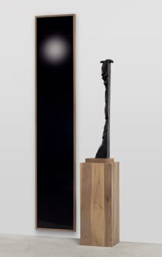 a black sculpture sitting on top of a wooden block next to a tall wall mounted mirror