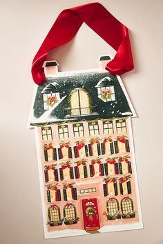 a paper doll house hanging on a wall with a red ribbon around it's neck