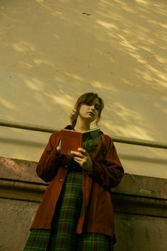 a woman standing in front of a wall holding a book