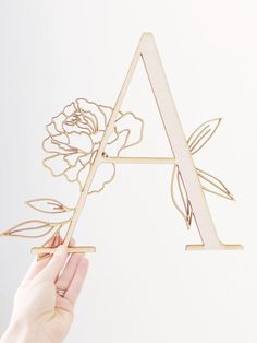 a person is holding up a wooden letter with flowers on the front and back sides