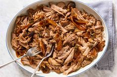 a bowl filled with meat and vegetables on top of a white table cloth next to a fork