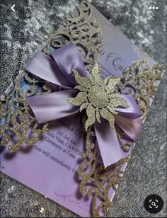 a purple and gold wedding card with a large bow on the front, sitting on top of glittery fabric