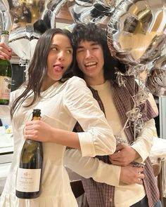 a man and woman hugging each other while holding bottles of wine in front of balloons