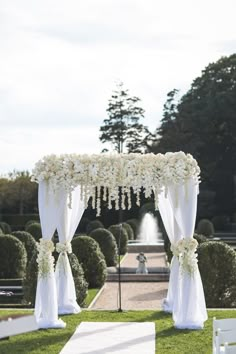 an outdoor wedding setup with white flowers and draping on the top, surrounded by greenery