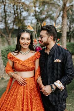 a man and woman standing next to each other in front of some trees wearing orange outfits