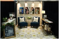 two blue chairs sitting in front of pictures on the wall and a table with flowers