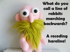 a pink stuffed animal with a green beard and mustache on it's head, sitting in front of a white wall