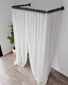 a white curtain with black beading hanging from it's side in front of a potted plant