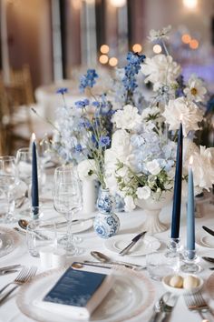 the table is set with blue and white flowers in vases, silverware, and candles