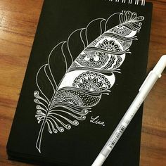 a black notebook with a white feather on it and a pen next to it, sitting on a wooden table