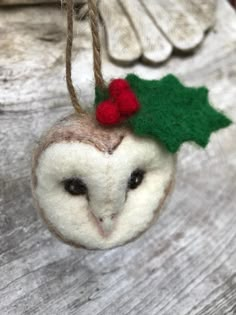 an owl ornament hanging from a rope on a wooden table with leaves and holly