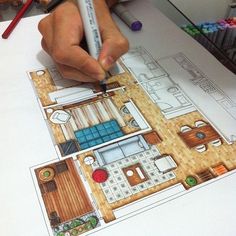 a person is drawing a floor plan with a pencil and colored crayons on the table