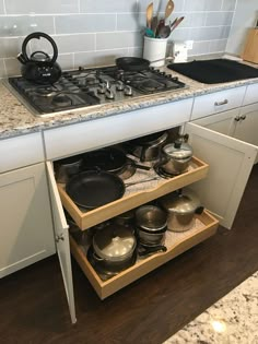 an open drawer with pots and pans on it in the middle of a kitchen